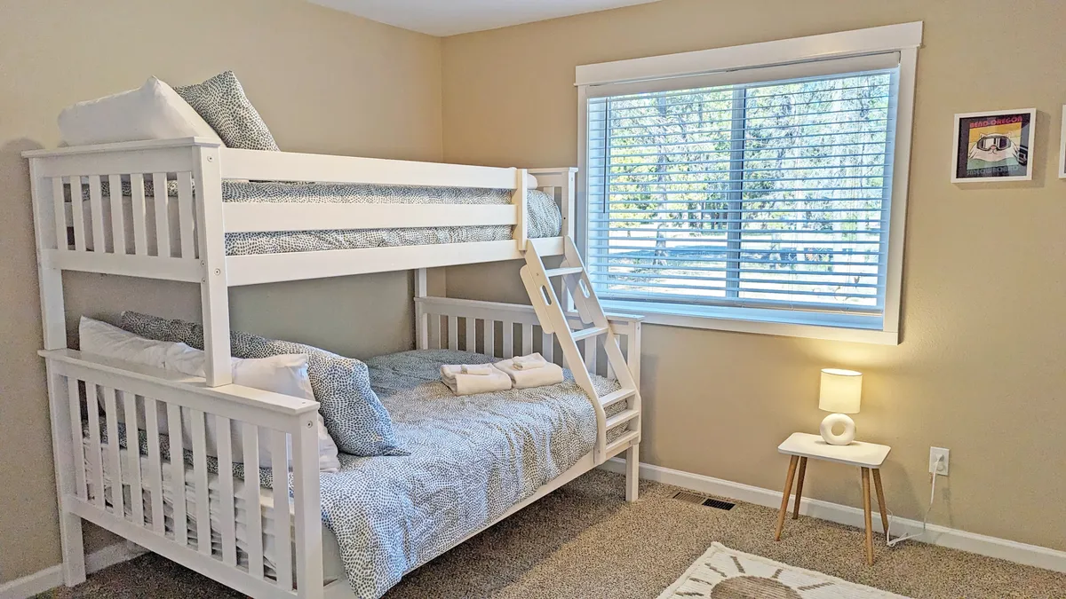 A playful and inviting bedroom with bunk beds positioned beside a window providing natural light, a small lamp for nighttime reading, and whimsical wall art. The setup is perfect for children, friends, or family members sharing a space, evoking memories of fun sleepovers and laughter.