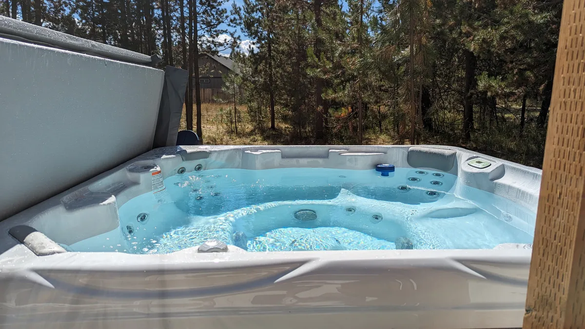 An outdoor hot tub framed by tall pine trees, with sparkling blue water inviting relaxation. The setting captures a tranquil, natural environment, perfect for family members to unwind together after a day of adventure.
