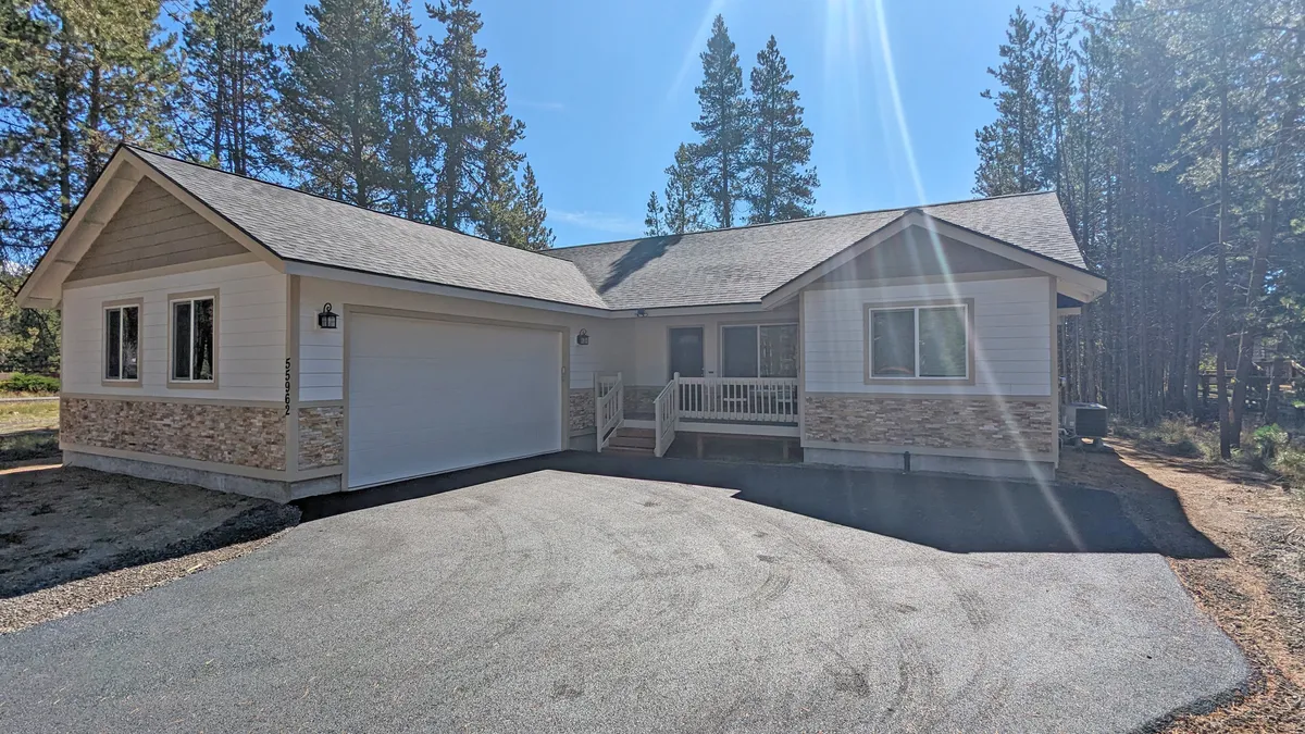 An inviting front porch framed by stone accents, large windows, and shaded by surrounding trees. The scene radiates calm and connection to the wooded environment, hinting at the natural trails and peaceful mornings described in the section.