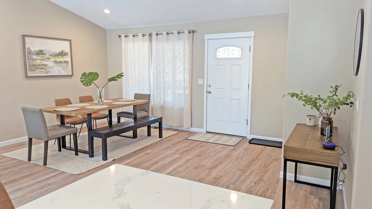 This image features a sunlit dining table set near an entryway, with elegant curtains and tasteful artwork. The space exudes warmth and provides a bright, comfortable atmosphere ideal for working remotely, enjoying meals, or simply relaxing during downtime.