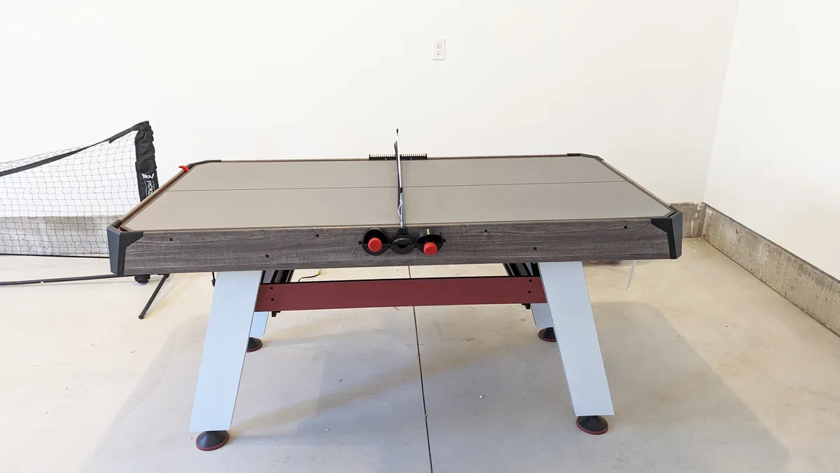 This image depicts an air hockey table set up in a garage or game area, with a visible goal net and space for active play. The environment feels inviting for group games and friendly competition.