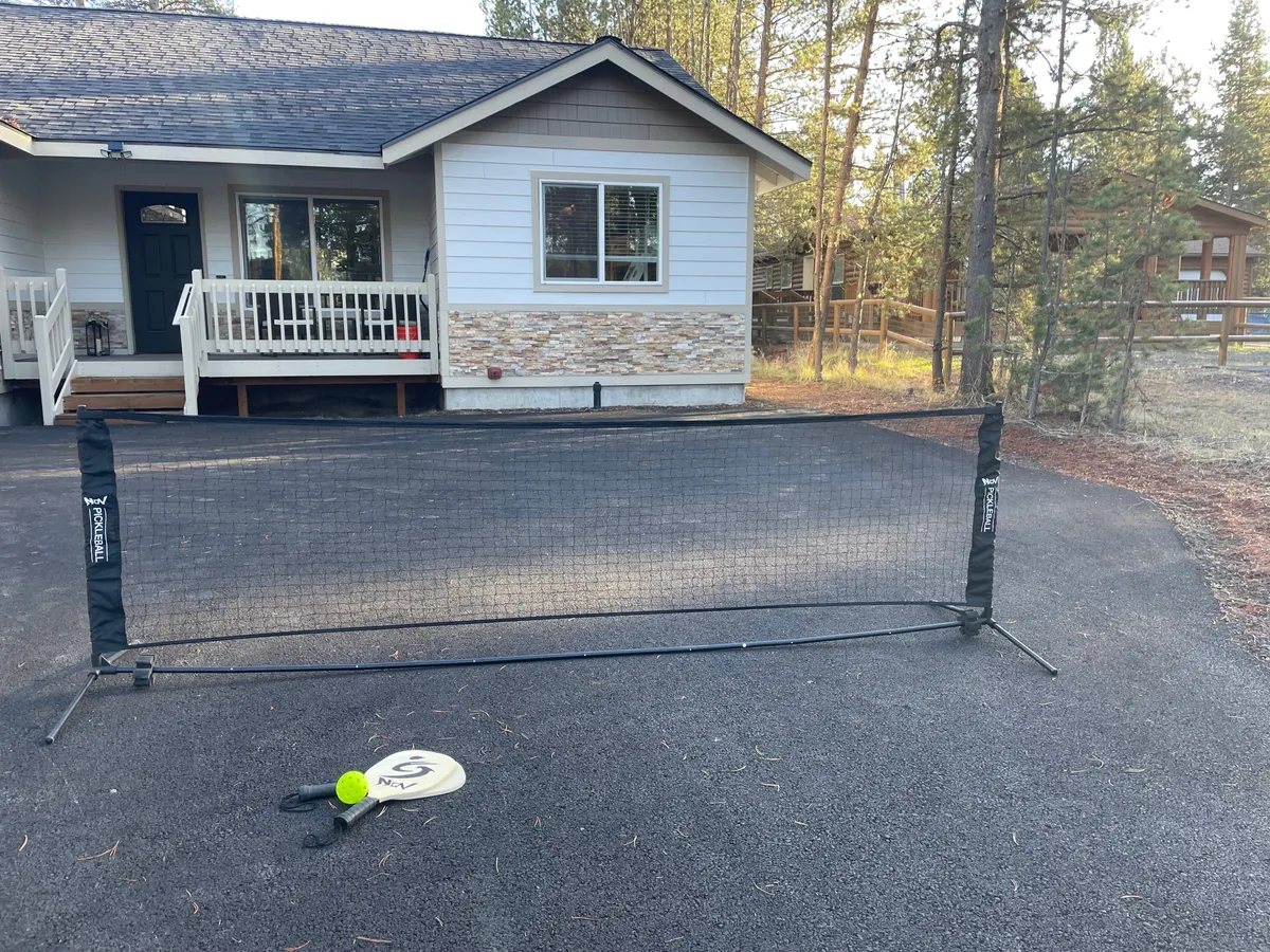 This exterior image showcases the front porch of the home, surrounded by tranquil greenery and featuring a tennis net with a paddle and ball. The inviting porch hints at a relaxing spot to unwind after work and the tennis setup illustrates recreational opportunities right outside the door.