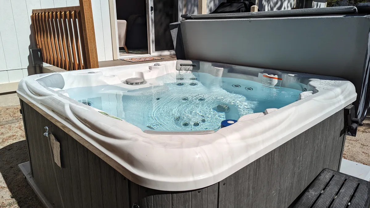 A private hot tub sits on a wooden deck, surrounded by natural wood and greenery. The water surface is inviting, and the deck offers space for relaxing and socializing, evoking a tranquil and luxurious outdoor retreat.